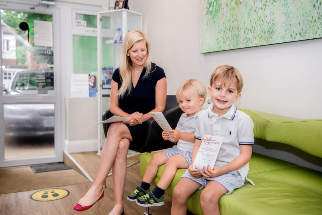 Image of a mother smiling sitting on a sofa with her two young sons. Children's dentist in Sutton at Sherwood Park Dental in Surrey.